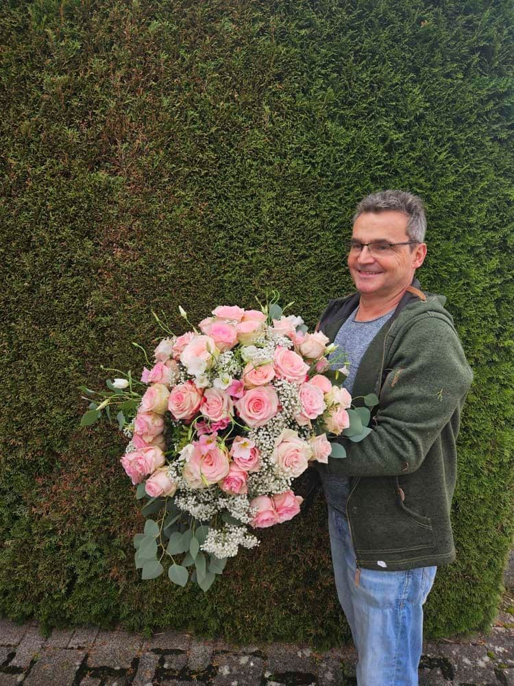 Florist von Vessa Floristik mit einem frisch gebundenen Rosenstrauß vor einer begrünten Wand
